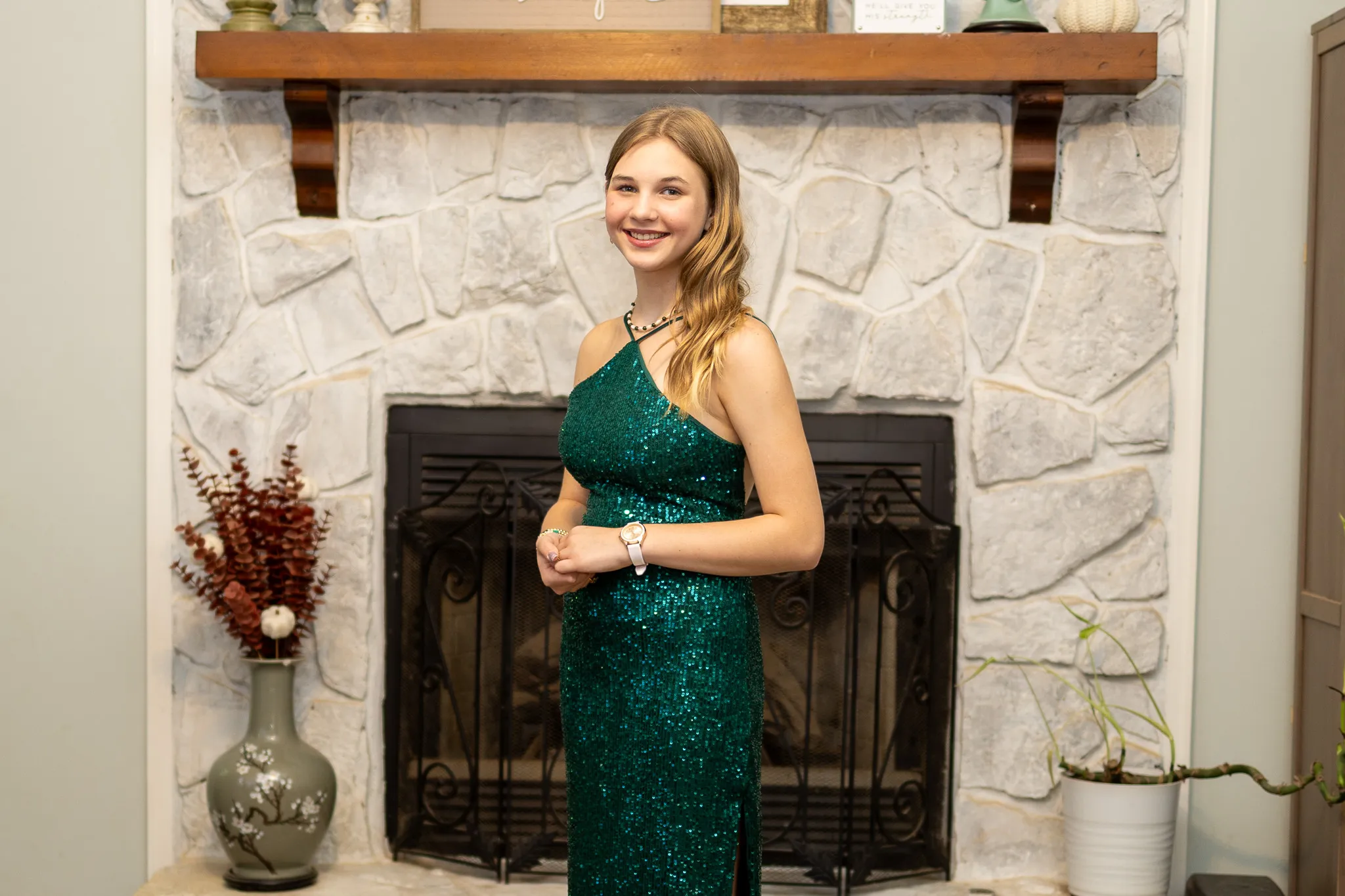 Young woman in formal dress smiling at camera in front of a fireplace